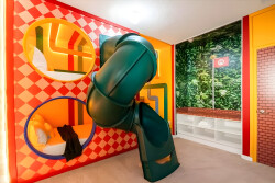 This vibrant playroom, with its whimsical green slide and bright red and orange patterns, offers an energizing atmosphere. Unique circular nooks add charm, providing endless fun for kids and a lively space for family gatherings.