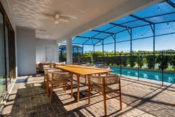 Dine outdoors on a covered patio with a large table, comfortable seating, ceiling fan, screened pool views, string lights, and peaceful greenery, creating a perfect space for vacation meals.