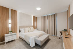 Experience a peaceful retreat with a plush king-size bed draped in soft linens, set against sleek wood paneling. Warm lighting creates an inviting ambiance, and an elegant desk provides a perfect space to plan your adventures.