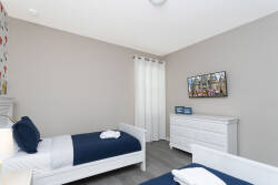 This cozy bedroom features two comfortable twin beds with crisp linens, soft gray walls for a calming atmosphere, and natural light through sheer curtains, creating a restful retreat enhanced by modern decor and tasteful artwork.