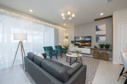 This bright living room boasts a plush gray sofa and vibrant teal chairs for a stylish contrast. Natural light streams through sheer curtains, creating an inviting space ideal for relaxation or socializing with friends.