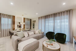 This stylish living area boasts a plush sectional sofa in soft neutrals, paired with inviting green accent chairs. Expansive windows let in natural light, enhancing the modern decor and creating a warm, welcoming atmosphere.