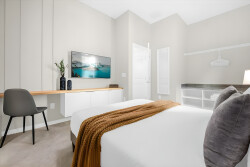 Relax in this cozy bedroom with its calming colors, a crisp white bed topped with a warm throw, a sleek desk for unwinding, and soft lighting paired with subtle wall art for a truly welcoming atmosphere.