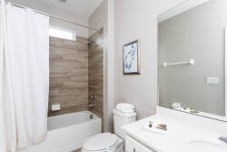 Step into this bright bathroom, featuring a sleek white vanity and a large mirror that amplifies the natural light. The warm wood paneling adds a touch of comfort, while plush towels are neatly arranged for your convenience.