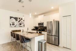 Cook and gather in a bright Mickey themed kitchen with white cabinets, stainless steel appliances, a large island, pendant lights, bar seating, and fun wall art, perfect for family meals during vacation.