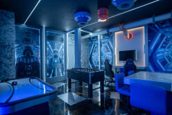 Experience a lively game room designed for fun, featuring a sleek foosball table and glowing blue accents. The cool, dark walls and modern furnishings create an energetic vibe perfect for friendly competition.