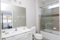 Bright and airy, this bathroom features a sleek glass shower and a spacious vanity topped with fresh greenery, offering a refreshing start to your day. Natural light pours in from the window, enhancing the clean, modern design.