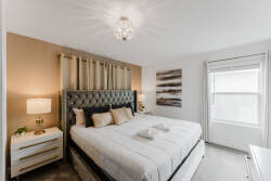 Unwind in this beautifully designed bedroom with a plush tufted headboard and soft, neutral bedding. The warm golden tones and elegant light fixture create a cozy atmosphere ideal for restful nights.