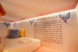Step into a whimsical nook featuring a cozy bed framed by a playful Cinderella mural, complete with soft lighting that creates a warm ambiance. Plush pillows in soothing hues invite you to relax and enjoy a fairy tale escape.