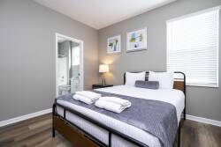 Enjoy restful nights in this thoughtfully designed bedroom with a plush queen bed, crisp linens, and cozy towels. Soft gray walls create a calming backdrop, while natural light fills the space, enhancing its inviting atmosphere.