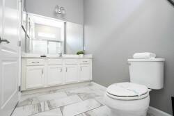 Enjoy a bright bathroom with sleek white cabinetry and elegant marble-style flooring. The spacious countertop and large mirror create a refreshing space for your morning routine, while a plush towel adds a cozy touch.
