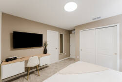 This cozy bedroom offers a sleek wall-mounted TV and a stylish desk, perfect for emails or planning your day. Soft beige tones and plush carpeting create a welcoming atmosphere, making it an ideal retreat for relaxation.