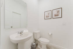Enjoy a bright and airy bathroom featuring a sleek white pedestal sink and streamlined toilet, enhanced by tasteful framed art for a sophisticated touch, all contributing to a fresh and comfortable ambiance.