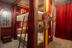 Step into this imaginative bunk room, where rich burgundy curtains frame cozy beds beneath rustic wooden beams. The playful design features a stained glass window, adding a whimsical touch to this unique space.