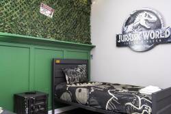 Experience a themed oasis with a vibrant green wall and playful dinosaur designs. The twin bed showcases a bold graphic print, ideal for adventurous guests, while a whimsical Jurassic World sign enhances the fun atmosphere.