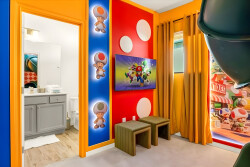 Welcome to a vibrant space with playful decor and cozy seating that invites relaxation. Bold orange and blue walls, adorned with whimsical art, are warmed by natural light filtering through sheer curtains, creating a delightful.