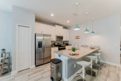 This bright kitchen boasts stainless steel appliances and a spacious light granite island. Blue pendant lights bring color above inviting bar stools, creating a perfect spot for casual meals and gatherings.