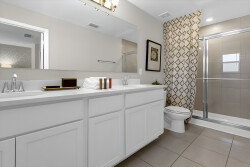 Experience a beautiful bathroom with sleek white cabinetry, warm beige tiles, and a stylish accent wall. The bright, airy space with abundant light and a modern walk-in shower offers a refreshing retreat during your stay.