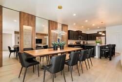 Share meals in a stylish dining area with a long wood table, black chairs, modern pendant lighting, mirrored wall accents, and easy access to the kitchen, creating a warm space for vacation gatherings.
