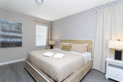 Awake in a serene bedroom with soft beige tones and a plush bed adorned with decorative pillows. Natural light streams through elegant curtains, creating a cozy atmosphere enhanced by stylish textured wall art.