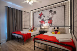 Bright and cheerful, this bedroom features two cozy beds adorned with bold red spreads, complemented by playful Mickey Mouse decor. The warm wood flooring and soft lighting create a welcoming atmosphere for a restful stay.