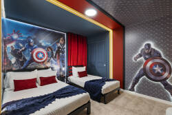 Rest in a bold superhero themed bedroom with two comfortable beds, vibrant wall art, red accents, and fun lighting. The dramatic decor creates an exciting space for kids and fans to enjoy during their vacation.