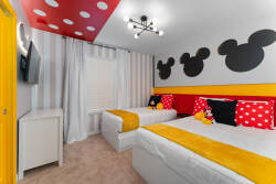This cheerful bedroom is bright and inviting, featuring two cozy beds with vibrant yellow throws and playful Mickey Mouse decor, all under a bold red ceiling with fun polka dots, making it perfect for a memorable stay for.