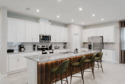 Experience a bright kitchen with elegant white cabinetry and a stunning gray and white marble island, ideal for casual dining. The warm wooden bar and stainless steel appliances ensure convenience for all your cooking endeavors.