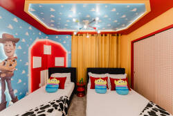 This cheerful children's room boasts bright colors and playful decor, featuring two cozy beds with vibrant bedding and fun character pillows, complemented by lively wall art and plenty of light for both play and rest.