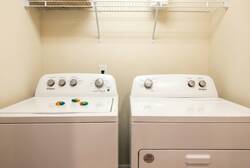 Take care of laundry with ease in a practical laundry area featuring a washer, dryer, storage shelf, and clean neutral space, adding comfort and convenience during your vacation.