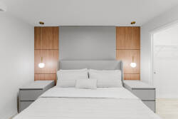 Step into a restful haven with a plush queen bed framed by sleek gray and warm wood accents. Soft, ambient lighting from stylish sconces creates a cozy atmosphere, perfect for unwinding after a day of exploration.