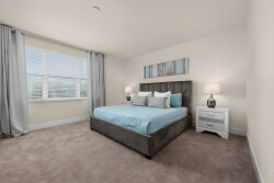Bathe in natural light in this cozy bedroom, featuring a plush grey upholstered bed adorned with soft blue linens. The neutral walls and warm carpet provide a comforting backdrop, while the modern artwork adds a touch of style.
