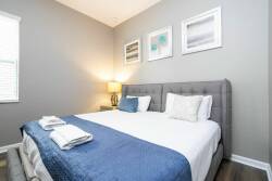Experience a peaceful bedroom featuring soft gray walls and tasteful art for a calming atmosphere. The plush tufted headboard pairs perfectly with crisp white linens and a cozy blue throw, while soft bedside lighting encourages.