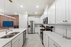 Cook with ease in a bright modern kitchen with white cabinets, stainless steel appliances, spacious counters, a large island, soft lighting, and an open view to the living room, perfect for family meals during vacation.