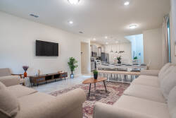 This bright and spacious living area boasts a soft beige sectional couch and a striking patterned rug, creating a cozy ambiance that invites relaxation and social gatherings, seamlessly flowing into the kitchen.