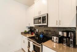 Cook with ease in a bright kitchen with white cabinets, stainless steel appliances, dark tile backsplash, countertop appliances, and plenty of storage, creating a practical space for family meals during vacation.