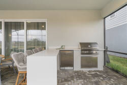 Enjoy a covered outdoor kitchen with stainless steel grill, pizza oven, sink, and sliding doors connecting to the living area, perfect for meals and relaxing outdoors.