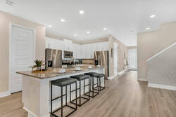 Cook and gather in a bright modern kitchen with white cabinets, stainless steel appliances, granite countertops, bar seating, recessed lighting, and warm wood flooring.