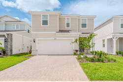 Experience a charming exterior with a light-hued facade and beautiful landscaping. The inviting paver driveway leads to a spacious garage, all set against sunny skies, creating a warm and welcoming atmosphere for your stay.