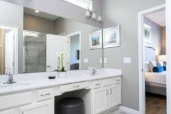 This bright and airy bathroom boasts a spacious double vanity with white cabinetry and sleek fixtures, enhanced by elegant artwork. Abundant natural light creates a tranquil ambiance, perfect for relaxation.