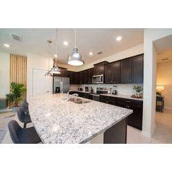 Cook in a bright kitchen with dark cabinets, granite counters, stainless steel appliances, a large island, pendant lights, bar seating, and an open view to the living area.