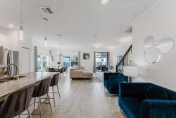 Experience a chic living area with cozy azure seating perfect for relaxation, complemented by elegant pendant lighting over a spacious kitchen island. Large windows fill the space with natural light, showcasing the modern decor.