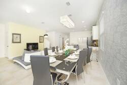 Experience a stylish dining area with a sleek glass table and contemporary gray chairs, perfect for gatherings. The textured accent wall and warm, inviting light fixtures add sophistication and charm to the space.