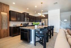 Cook and gather in a stylish kitchen with dark cabinetry, granite countertops, stainless steel appliances, a large island, black bar seating, and warm lighting, perfect for meals during your vacation.