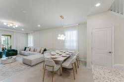 Enjoy a spacious living area with a cozy gray sectional and a stylish dining table for meals. Natural light fills the room, while a neutral palette and modern fixtures create a welcoming atmosphere for your relaxation.