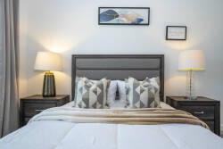 Enjoy peaceful nights in this beautifully designed bedroom, complete with a plush gray headboard, chic bedside lamps, and modern accent pillows.