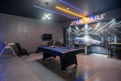 Step into a playful game room featuring a striking Star Wars mural that sets the stage for fun. The sleek pool table invites friendly competition, while vibrant neon lighting adds a dynamic touch to your leisure time.