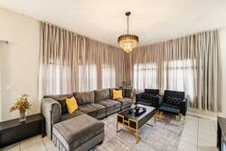 Welcome to this bright living room featuring a cozy gray sectional and stylish black armchairs. An elegant chandelier enhances the sophistication, while large windows bathe the space in natural light for a warm, inviting feel.