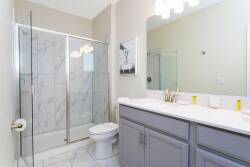 Bright and airy, this bathroom features sleek marble-patterned tiles and a spacious glass shower. The soft gray cabinetry complements the light fixtures, creating a fresh atmosphere that enhances your daily routine.
