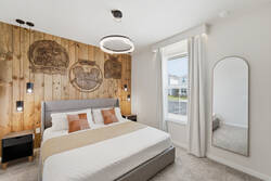 Rest in a stylish Mickey inspired bedroom with a cozy bed, wood accent wall, hanging lights, modern chandelier, soft white curtains, full-length mirror, and warm neutral details, creating a comfortable space for vacation